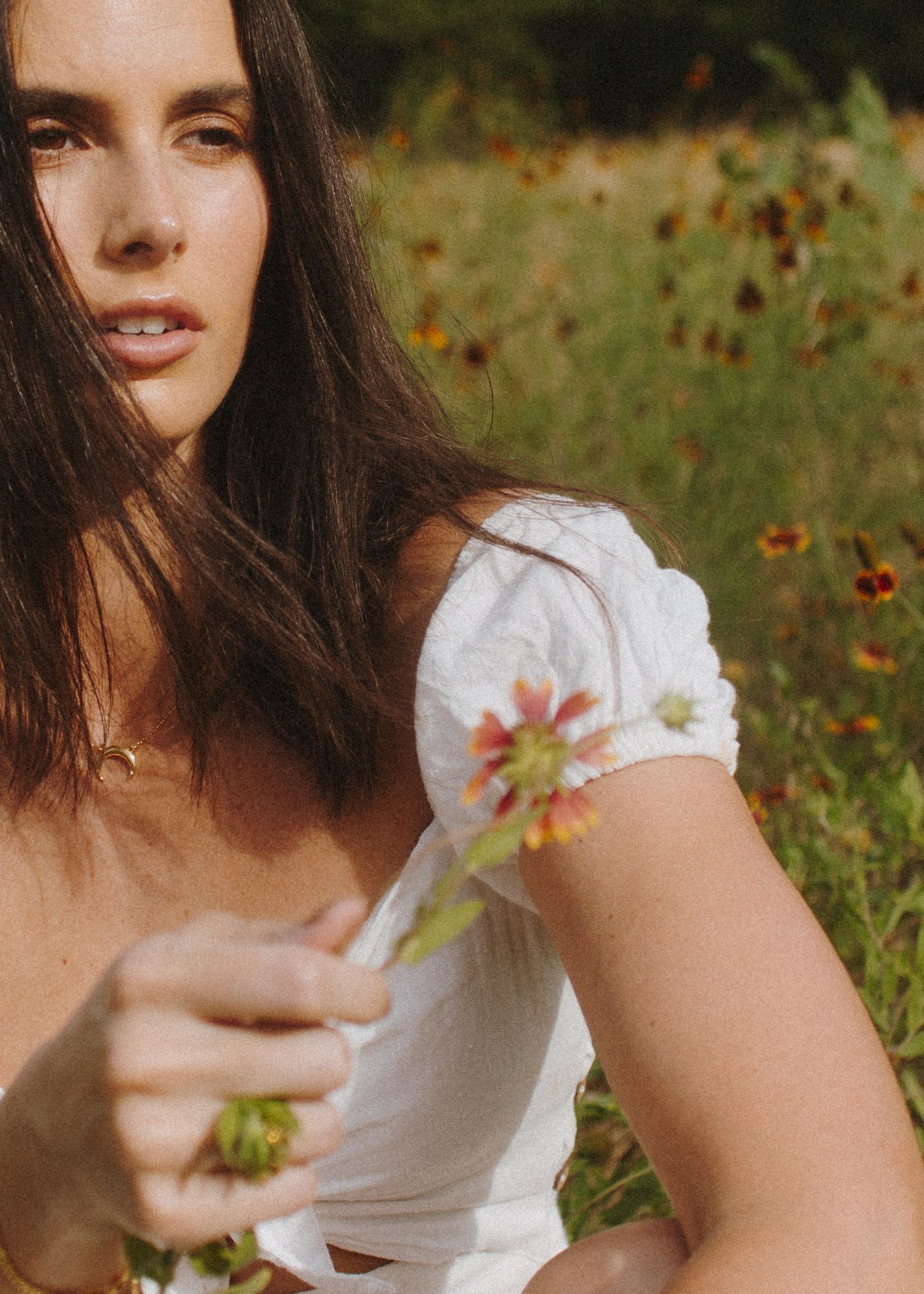 Romantic portrait of woman in white dress holding wildflowers in a summer meadow.