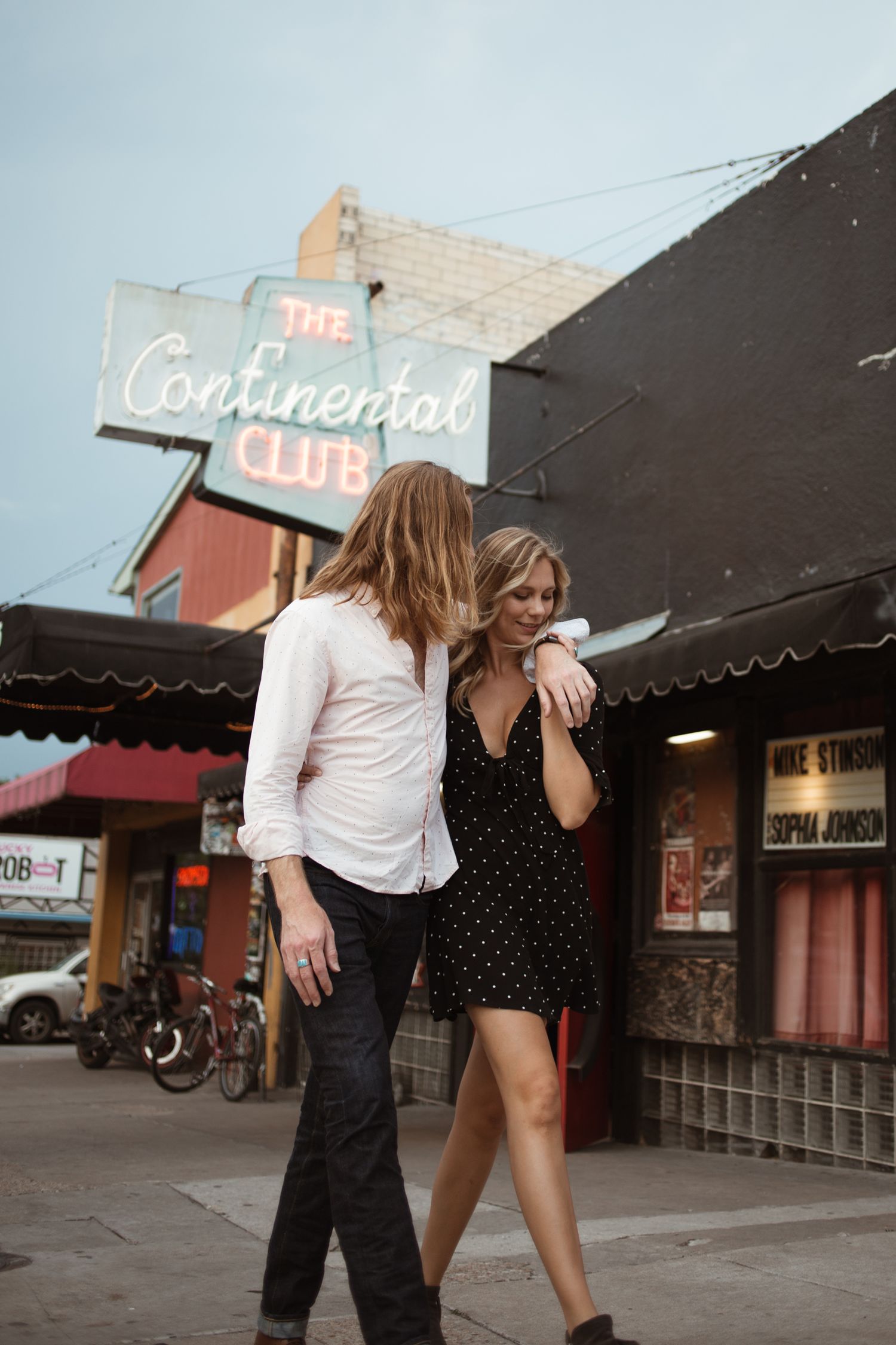 Couple sharing playful moments outside vintage storefronts with neon signs.
