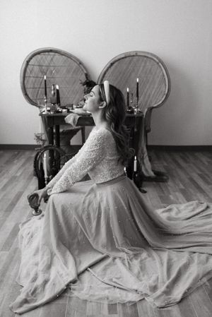Black and white portrait of a bride in a lace gown seated gracefully against vintage chairs.