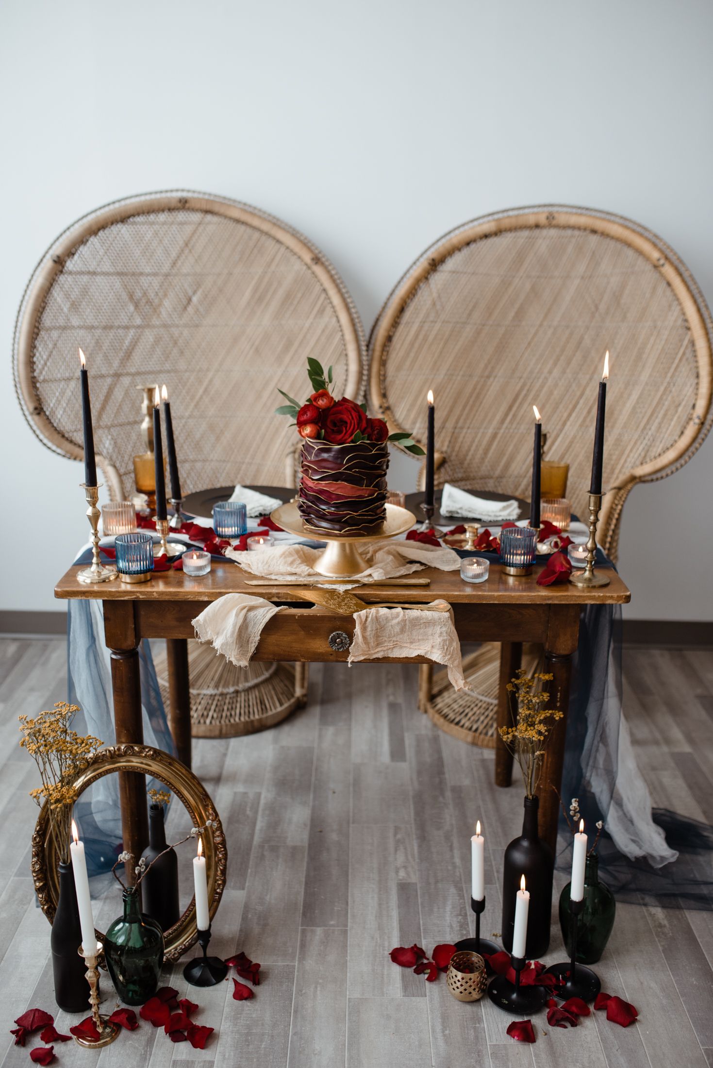 An elegant tablescape with wine barrel backdrops, black candles, and red floral centerpiece.