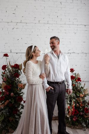 A couple shares a happy moment against a white brick wall decorated with red roses.