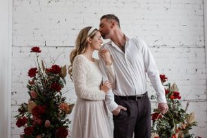 Intimate portrait of couple with red rose decorations against white brick wall background.