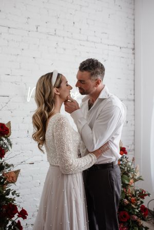 A romantic moment between a couple against a white brick wall with red floral decorations.