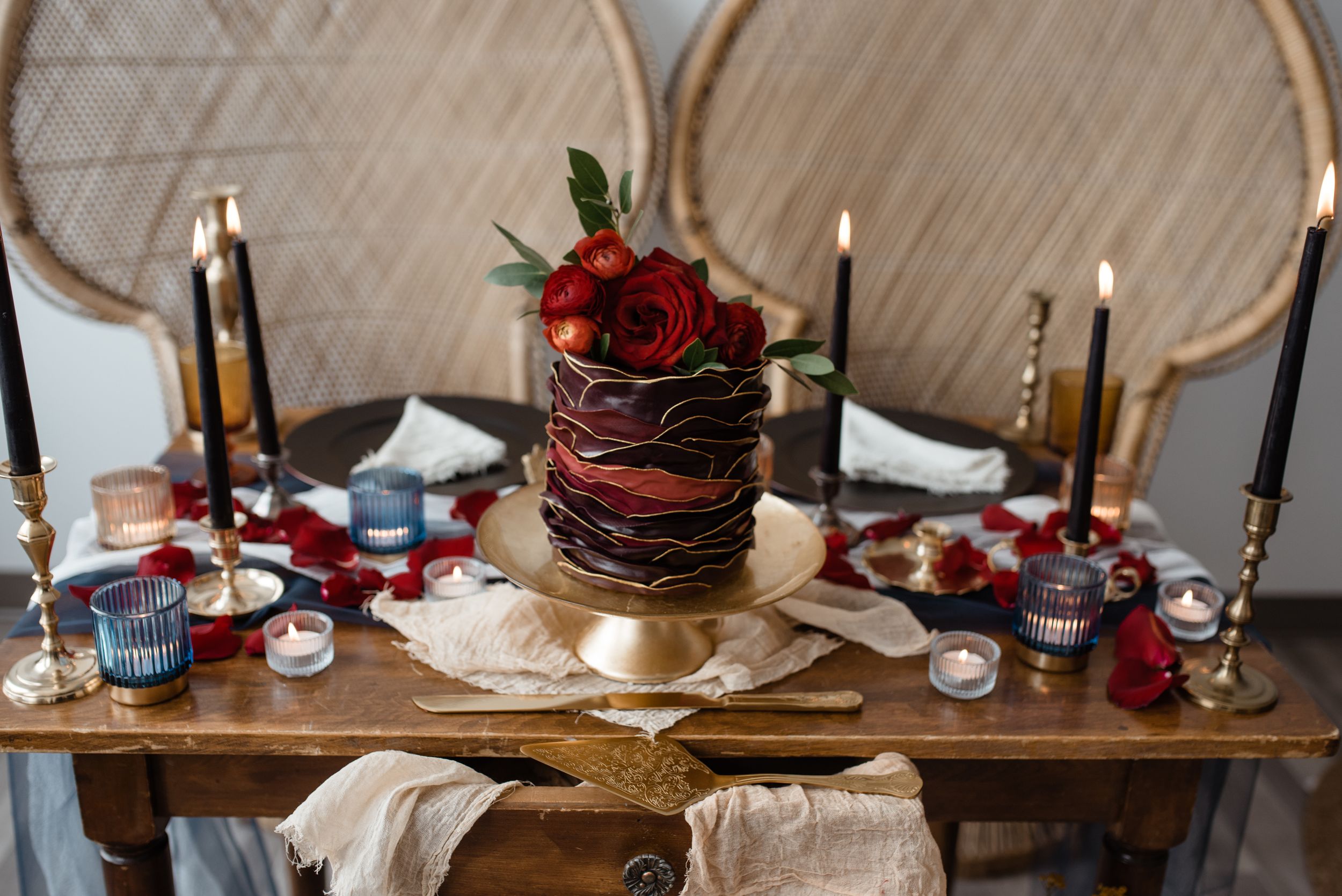 Elegant wedding table setting with dark cake, red roses, and gold candle holders.