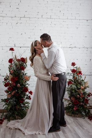 Romantic wedding portrait with red floral arrangements against white brick wall.