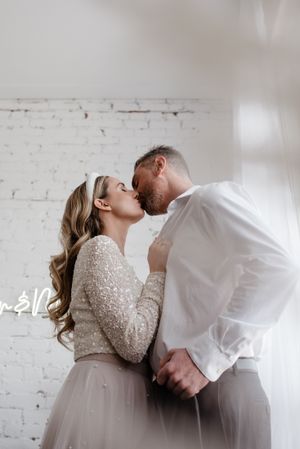 Romantic moment between couple against white brick wall, bride in sparkly long sleeve dress.