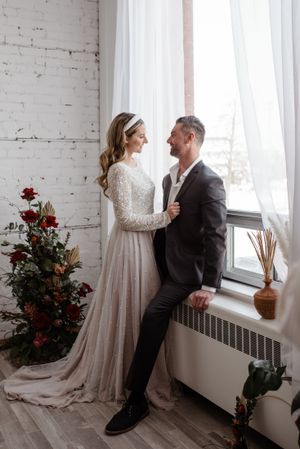 Elegant wedding portrait by window with long-sleeved lace gown and winter light.