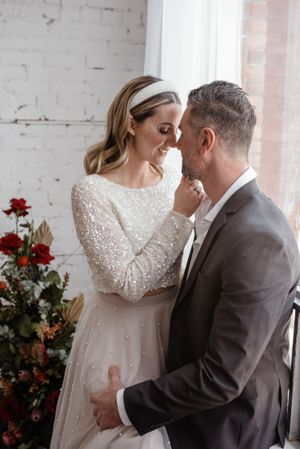 Intimate wedding portrait with couple sharing tender moment by bright window.