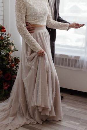 A detailed view of a sparkling long-sleeved wedding dress with pearl embellishments and flowing tulle skirt.