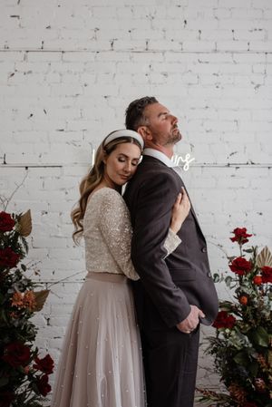A romantic portrait against white brick wall with red floral arrangements.