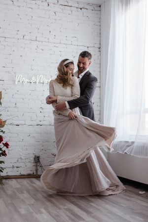Joyful dancing moment captured in white studio with flowing wedding dress and brick wall backdrop.