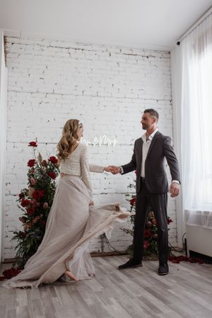 Couple dancing in white studio with brick wall backdrop and red floral arrangements.