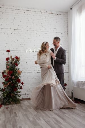 Romantic wedding portrait against white brick wall with red floral arrangement and neon sign.