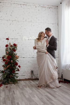 A romantic wedding scene with red roses against a white brick wall.