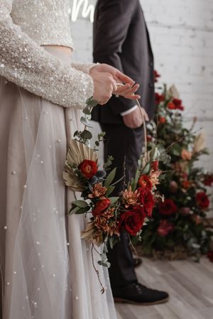 Detail shot of a red rose bouquet with long stems against a white dress and dark suit.