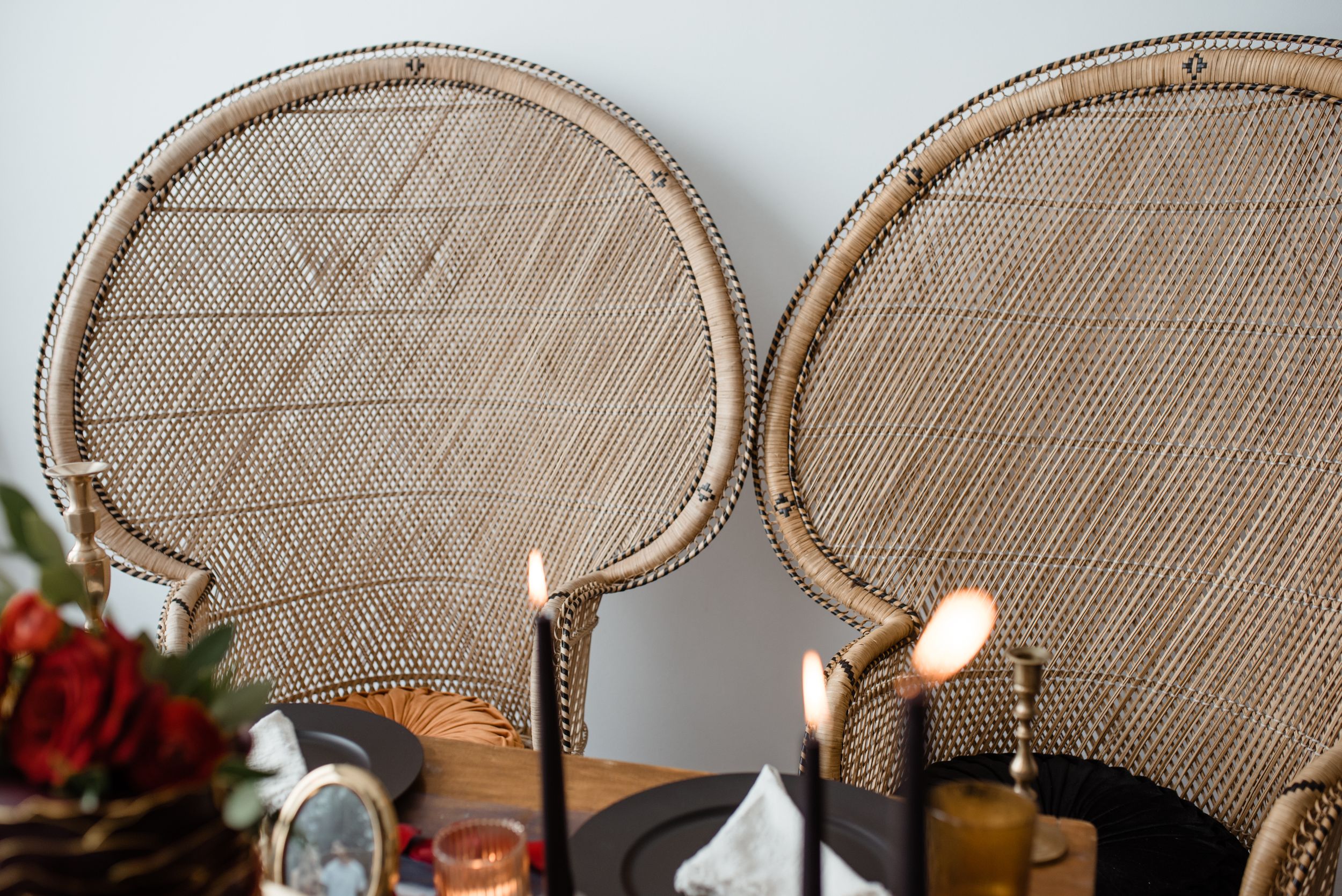 Elegant rattan peacock chairs with lit candles and floral decorations for wedding reception.