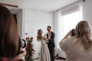 A wedding photographer captures a couple's intimate moment against a white brick wall.