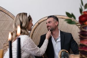 Intimate couple moment captured in peacock chair with romantic lighting and floral backdrop.