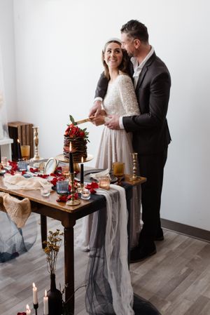A couple share a romantic moment at a table decorated with red flowers and candlelight for an intimate celebration.