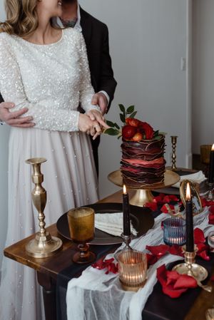 Elegant wedding table setting with a dark red tiered cake and candlesticks on a wooden surface.