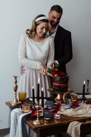 Couple sharing intimate moment while cutting chocolate wedding cake surrounded by elegant table decor.