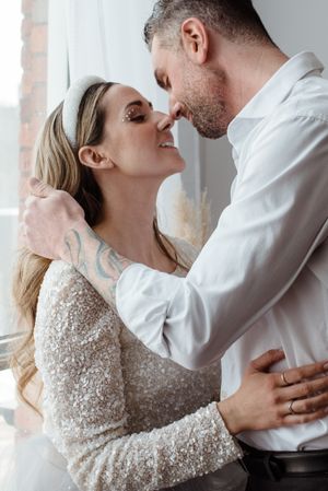 Intimate wedding portrait with lace dress and white button-down shirt against a bright window.