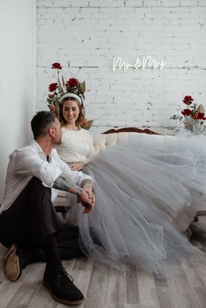 A romantic moment captured against a white brick wall with red floral accents and neon signage.