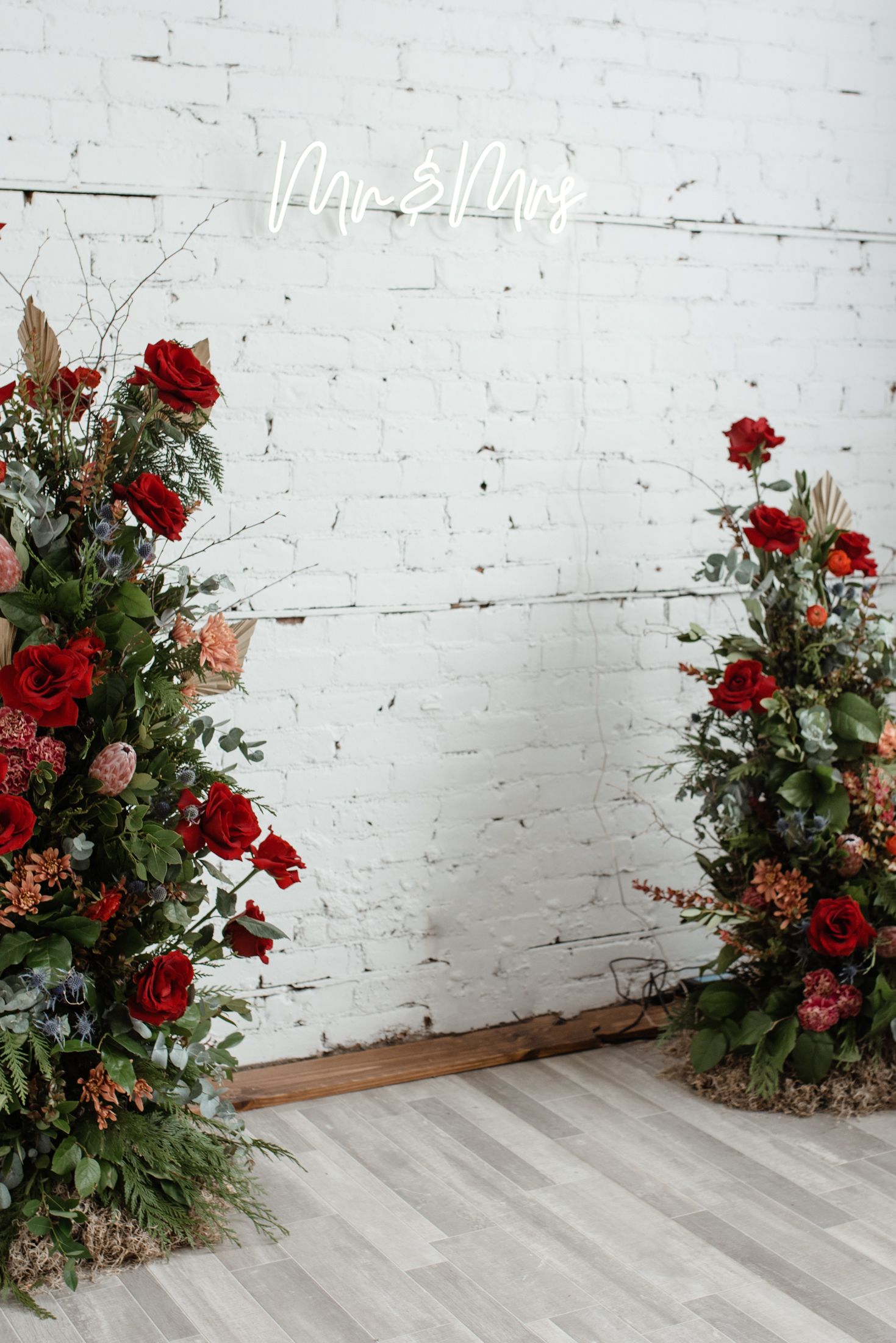 Modern wedding decor featuring two lush red rose floral arrangements against a white brick wall.