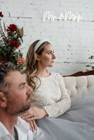 Elegant bridal portrait on white couch with red roses and Mr & Mrs sign on brick wall.