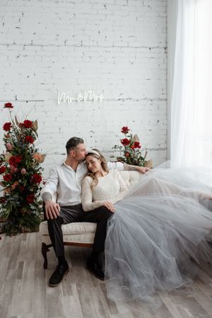 Romantic wedding portrait against white brick wall with red rose arrangements.