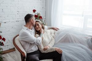 Intimate moment captured in light-filled room with white brick wall and red floral accents.