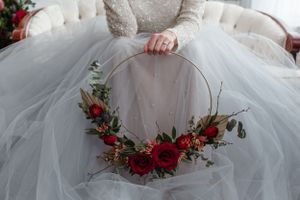 Floral hoop with red roses and greenery resting on tulle wedding dress.