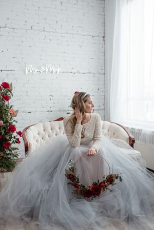 A romantic bridal portrait featuring a tulle gown and red floral accents against a white brick wall.