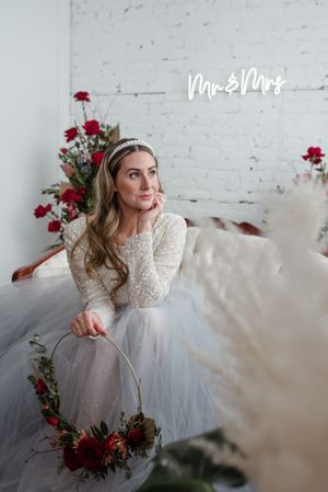 A winter bridal portrait with red roses and a Mr & Mrs sign against a white brick wall.