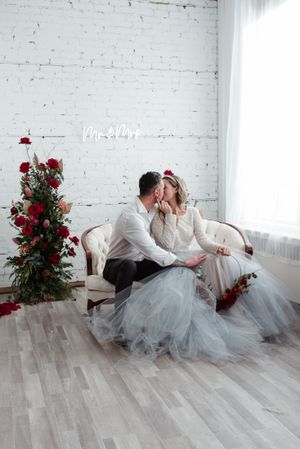 Elegant wedding portrait on vintage sofa with flowing tulle gown and red roses.
