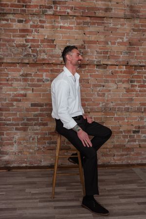 Person in white shirt sitting on wooden stool against exposed brick wall.