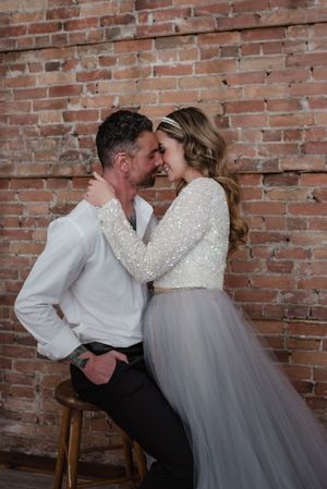 Romantic portrait against exposed brick wall featuring elegant tulle dress and intimate embrace.