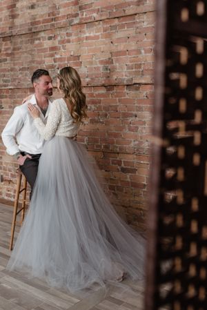 A romantic moment captured near a rustic brick wall with a flowing tulle gown.