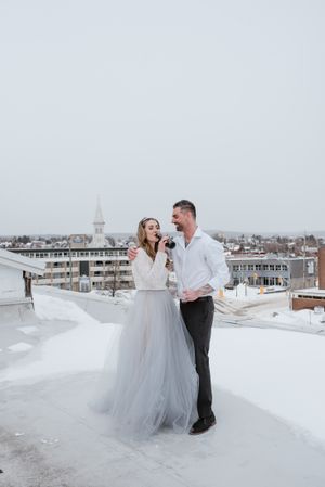 A winter rooftop portrait with a city skyline and church steeple in the background.