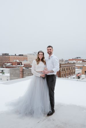 Winter rooftop wedding portrait with couple in formal attire against urban skyline.