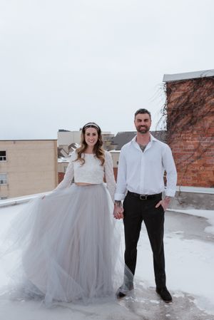 A couple in wedding attire poses on a rooftop with brick buildings in the background.