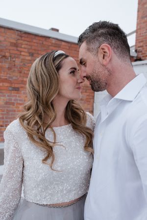 Intimate moment between couple in bridal attire against brick wall backdrop.