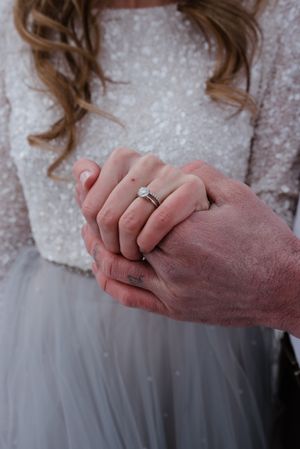 Close-up shot of hands with engagement ring against a backdrop of white lace and tulle.