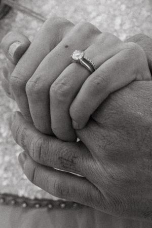 Black and white close-up of engagement ring while couple holds hands.