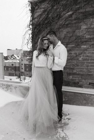 A couple in wedding attire shares a tender moment against a brick wall on a rooftop.