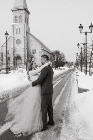 A romantic winter wedding photo in front of a church with snow-covered street lamps.