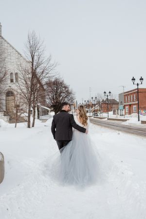 Couple walking down a snow-covered small town street lined with lampposts.