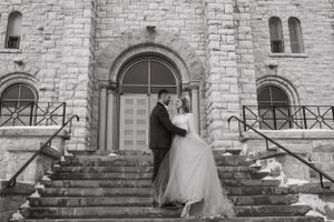 A classic black and white wedding photo on stone church steps with Gothic architecture.