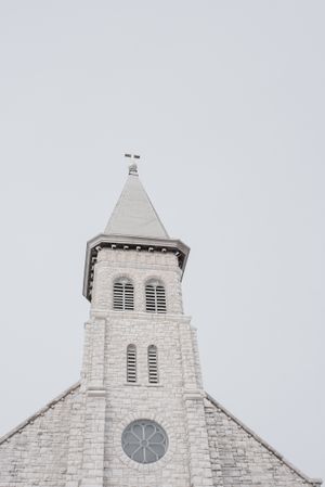 White stone church steeple with clock and architectural details against grey sky.