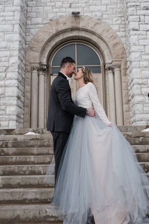 Intimate wedding moment captured on stone church steps with classic arched doorway backdrop.